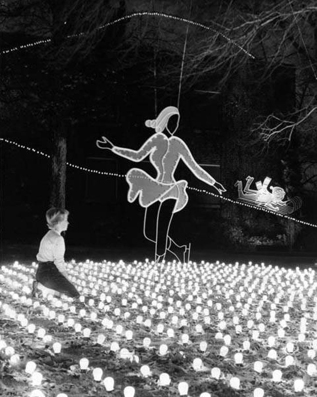 Christmas Display at Nela Park includes a figure skater gliding on frozen pond of lights while a bobsledder in the background takes a ride down a hill of lights, 1958.