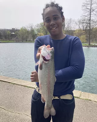 Boy wearing a long sleeved blue shirt and jeans hold a trout.