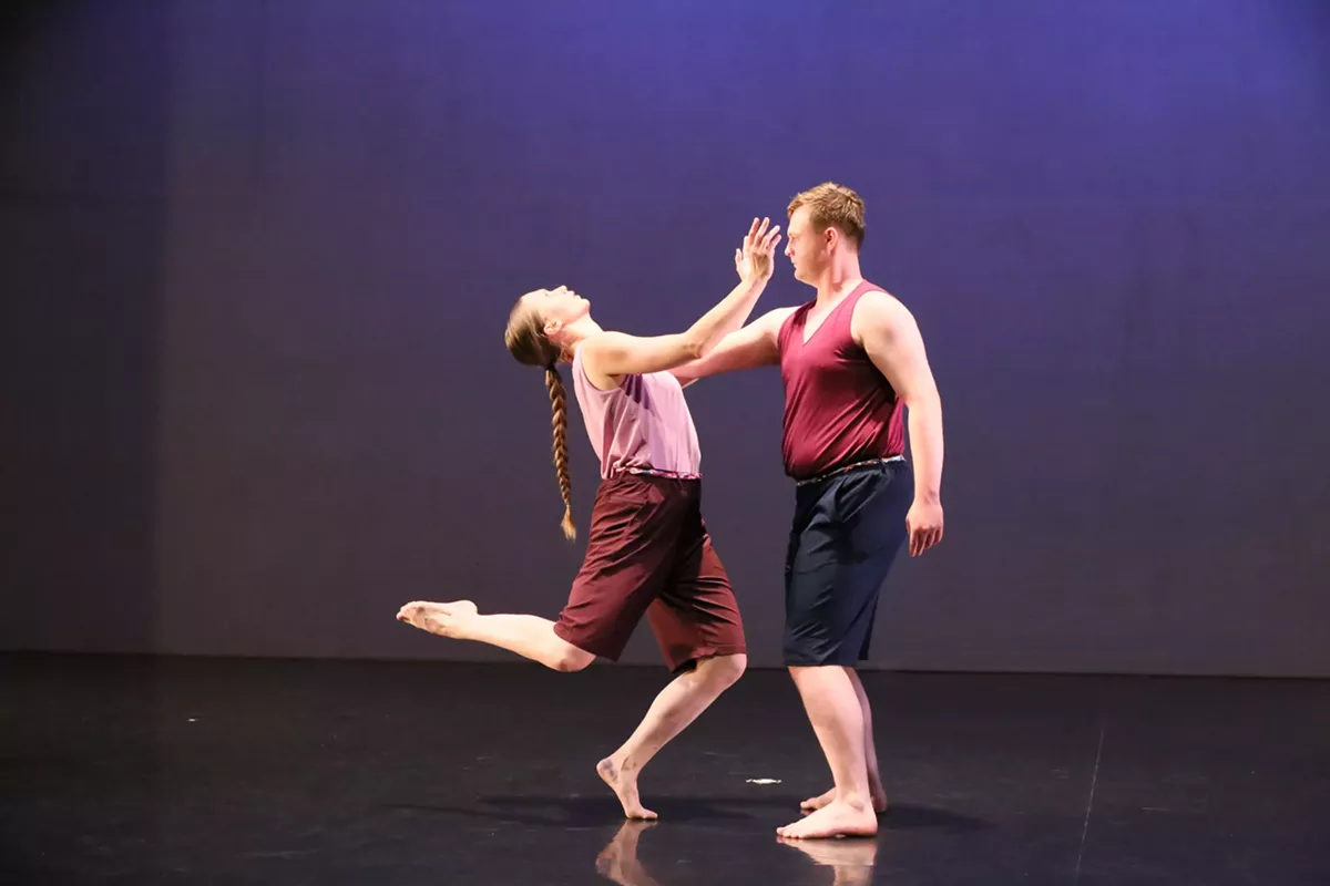 Two dancers face one another, one is being pushed back to balance on one leg.