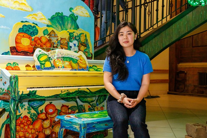 Chi-Irena Wong, 25, sits on the bench of the piano she painted for Midtown Cleveland. Wong's numerous murals in the neighborhood have helped Asiatown's visibility. Wong said there's a long way to go. "It's very muted" still, she said of the streets. - Mark Oprea