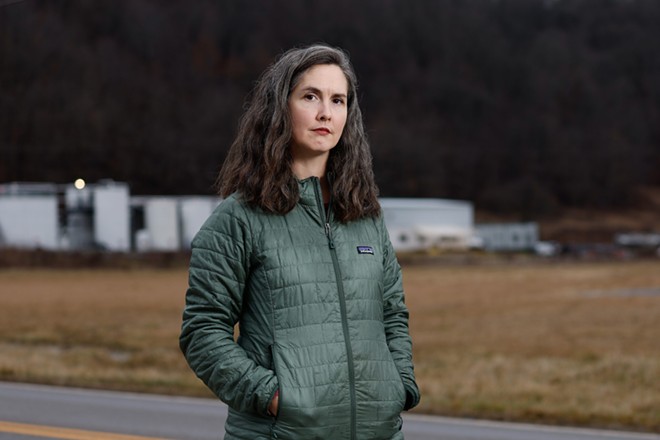 COSHOCTON, OH — JANUARY 25: Lucy Bryan Malenke, a freelance writer and local resident, with the white buildings and tanks of the Buckeye Brine injection facility on Airport Road in the background, January 25, 2024, in Coshocton, Ohio. - (Photo by Graham Stokes for Ohio Capital Journal)